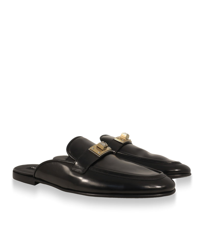 Dolce & Gabbana Mules in Schwarz mit goldfarbener DG-Logoplakette, Schrägansicht
